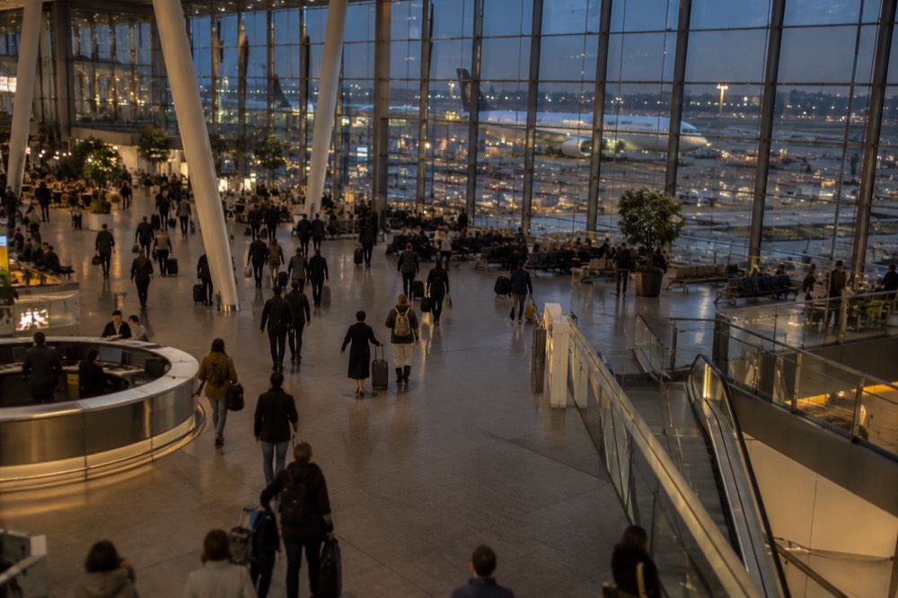 A wide view of Schiphol Airport's departure hall with airline signs and travellers with luggage