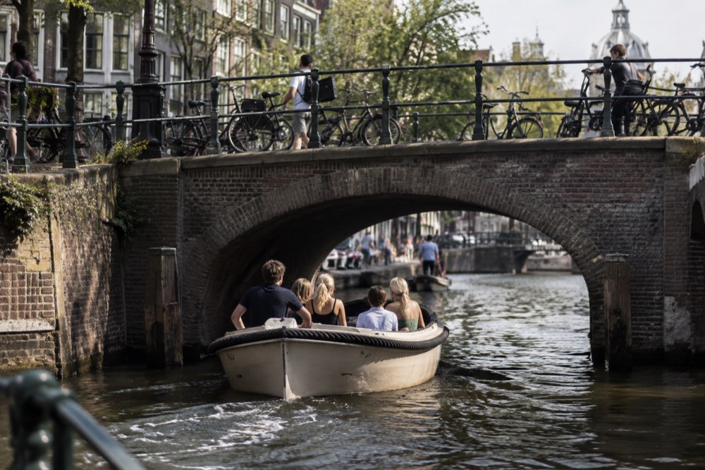 An open sloop passing under a narrow brick canal bridge in Amsterdam