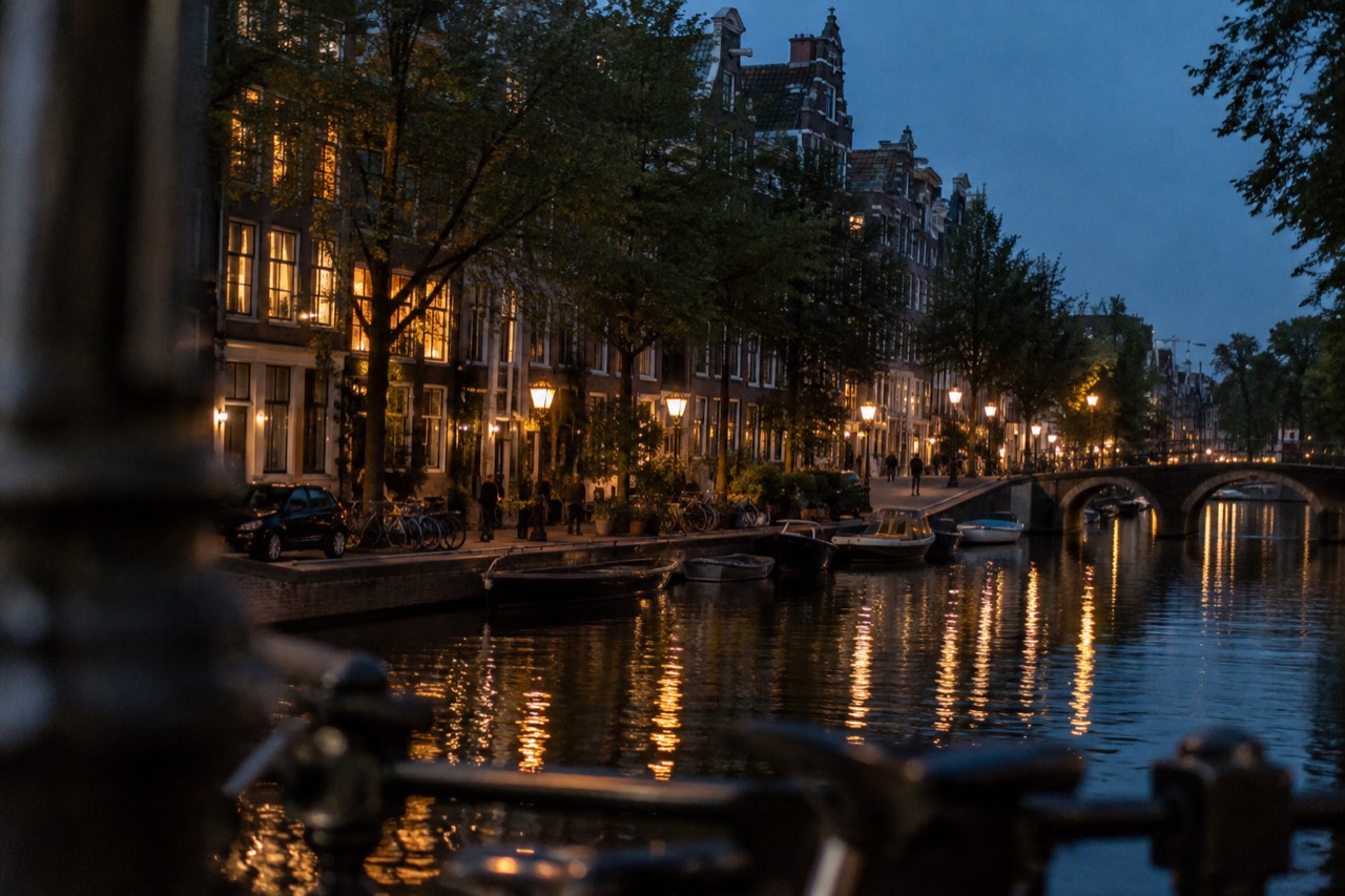 Amsterdam canal lined with trees and gabled houses under a clear summer sky