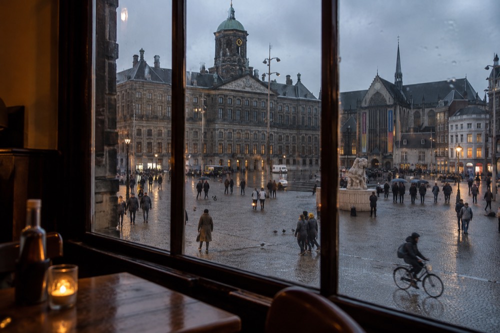 A warmly lit Amsterdam brown café interior with wooden tables and a low bar on a dark evening