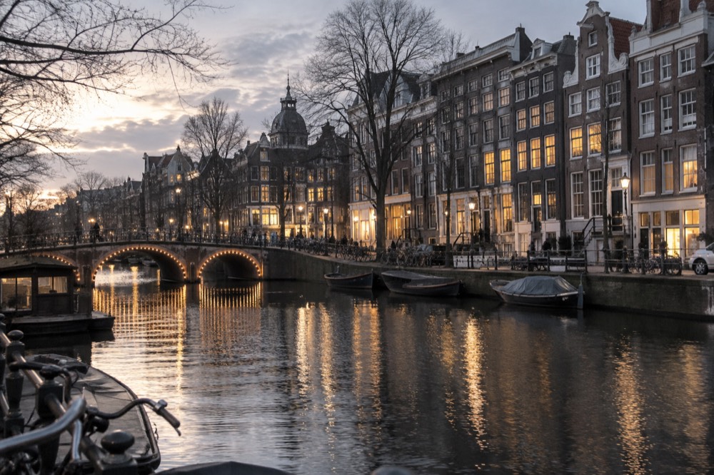 Illuminated canal houses and a lit bridge reflecting in dark water on a winter evening