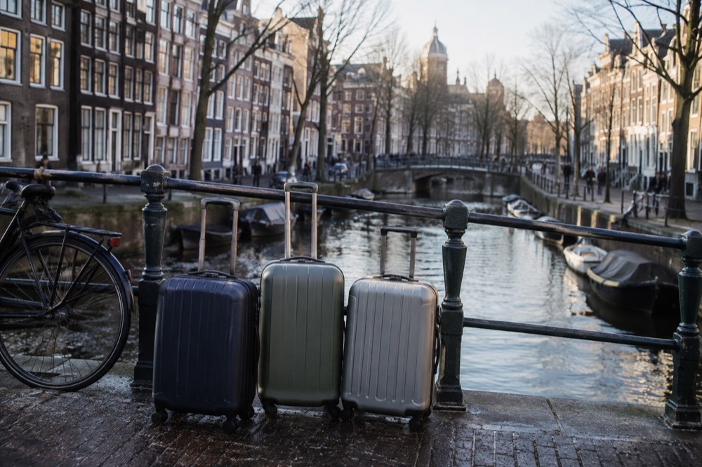 Suitcases standing on a canal bridge in Amsterdam with gabled houses along the water