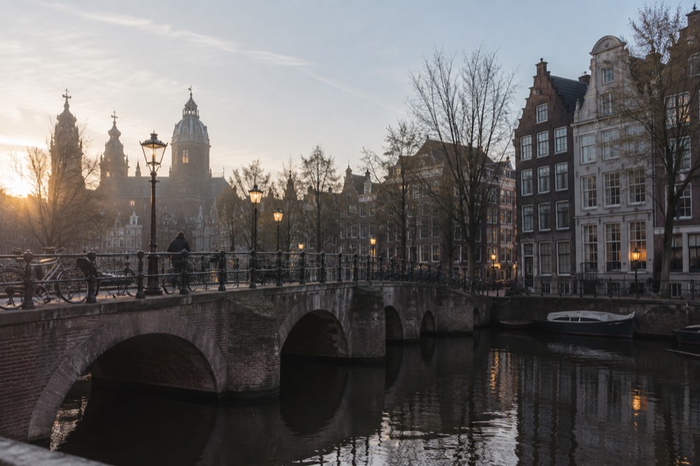 A canal bridge lit by warm street lamps above dark water with historic gabled houses in the background