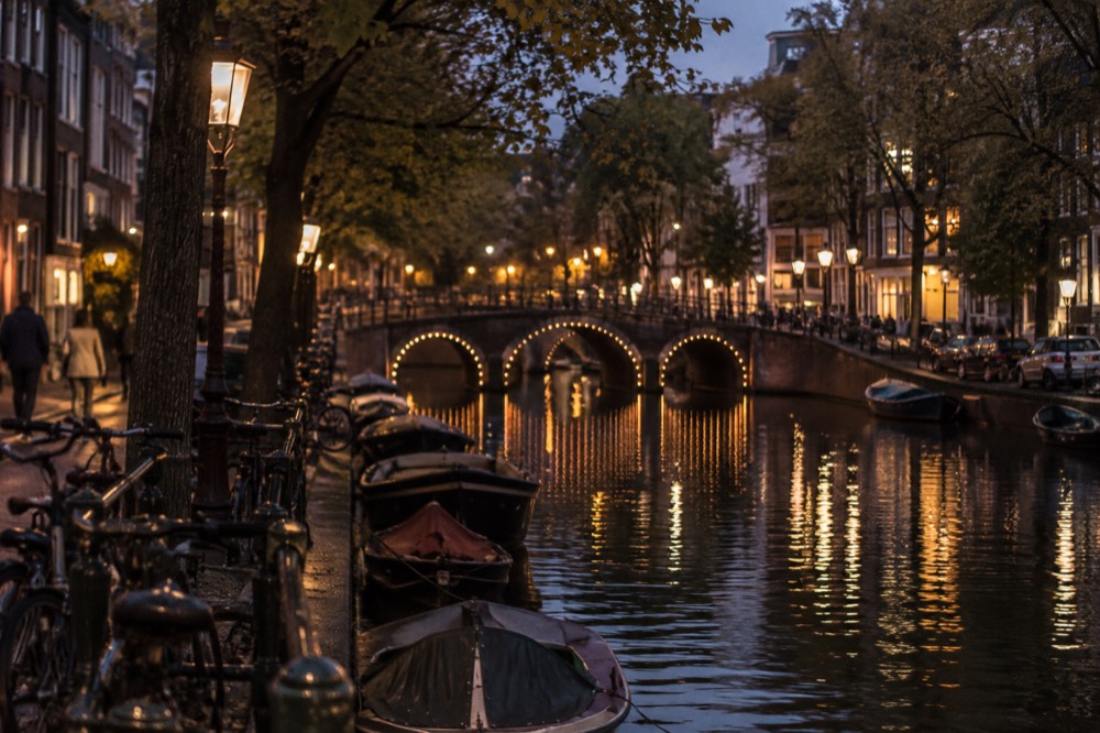 A narrow Amsterdam canal with trees along the quay and a bridge crossing the water