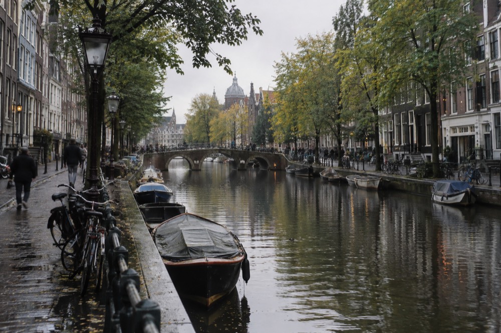 A long canal lined with trees and gabled brick houses curving away toward a stone bridge