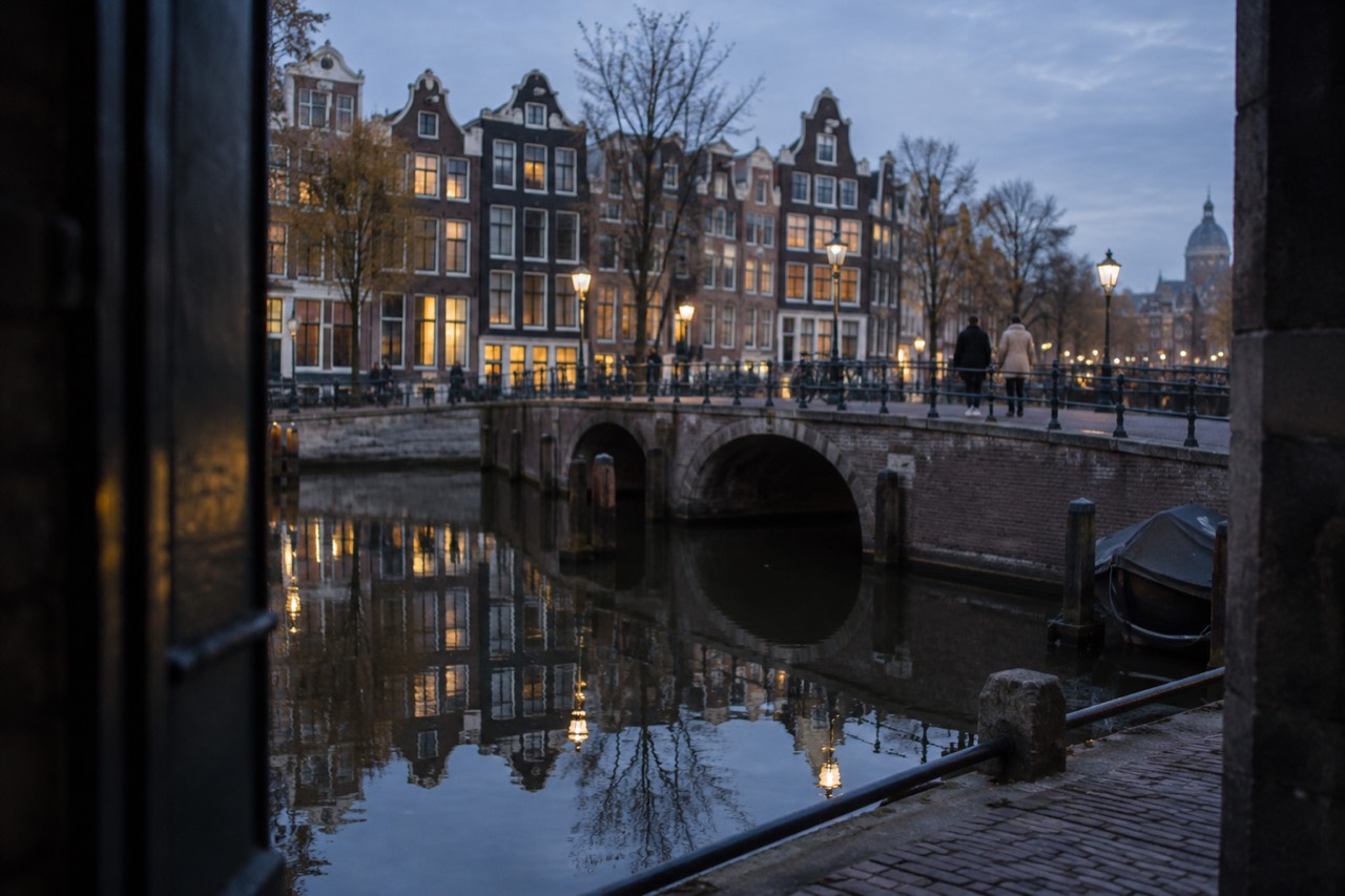 “Canal houses reflected in still water beside a stone bridge in Amsterdam”