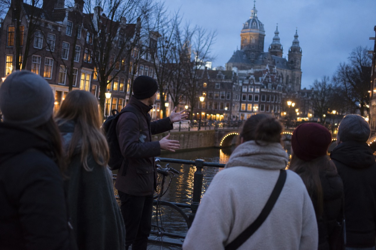 A guide speaking to a small group beside a canal bridge in central Amsterdam