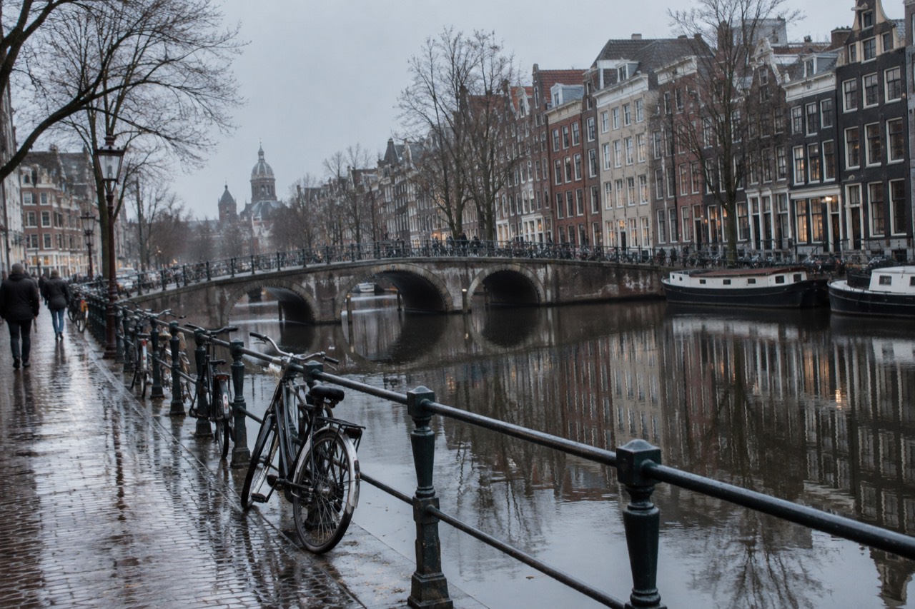 Amsterdam canal houses and bridge reflected in still water under a soft grey sky