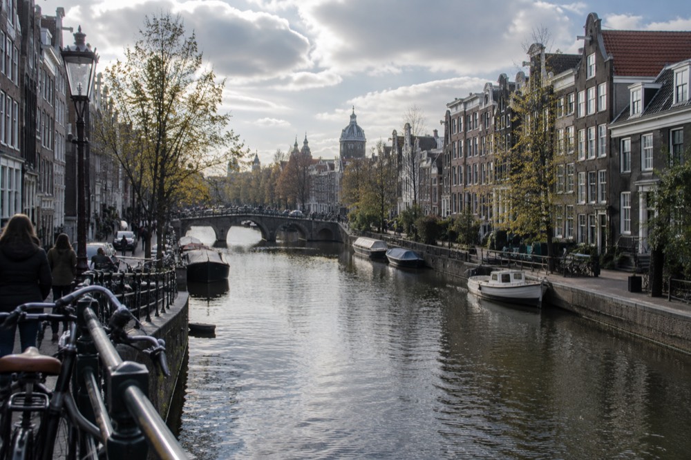 A quiet Amsterdam canal lined with narrow gabled houses and bicycles on a bridge