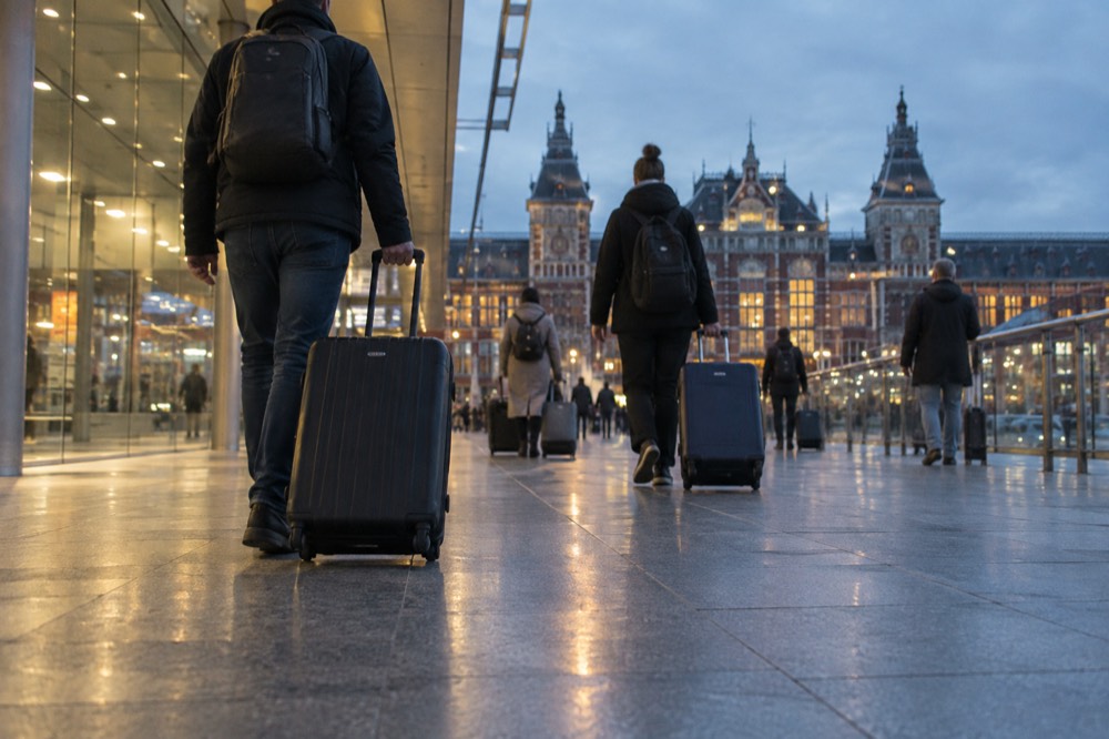 Travellers with suitcases walking through a bright airport terminal corridor towards a rail station entrance