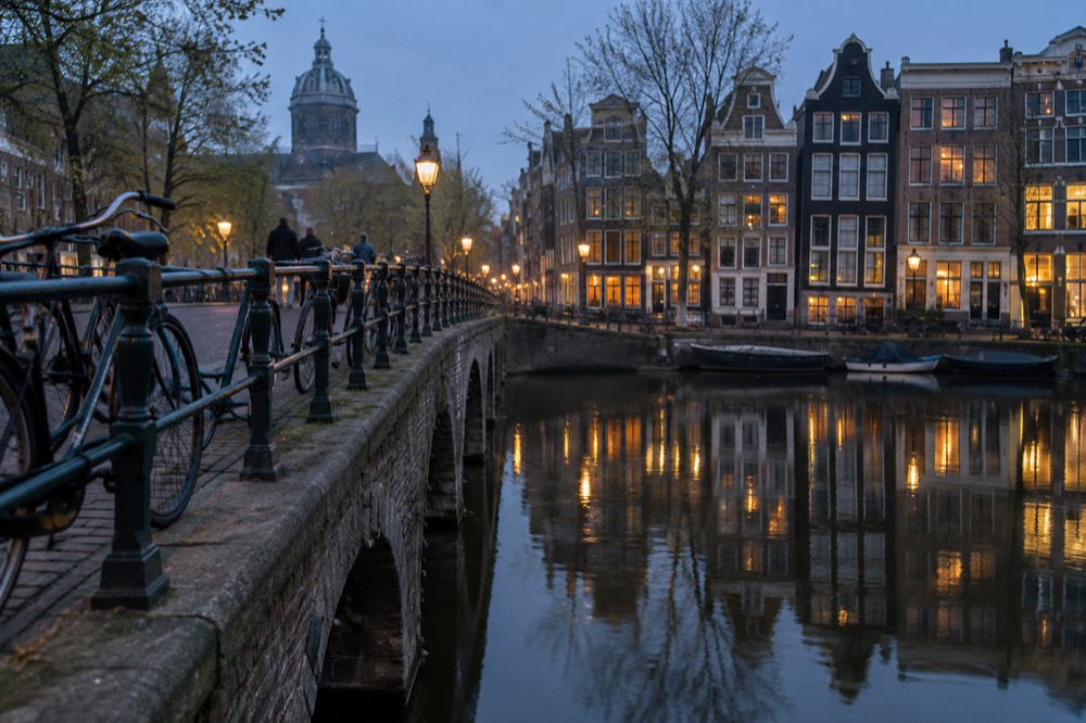 Amsterdam canal houses reflected in still water with bicycles parked on a stone bridge