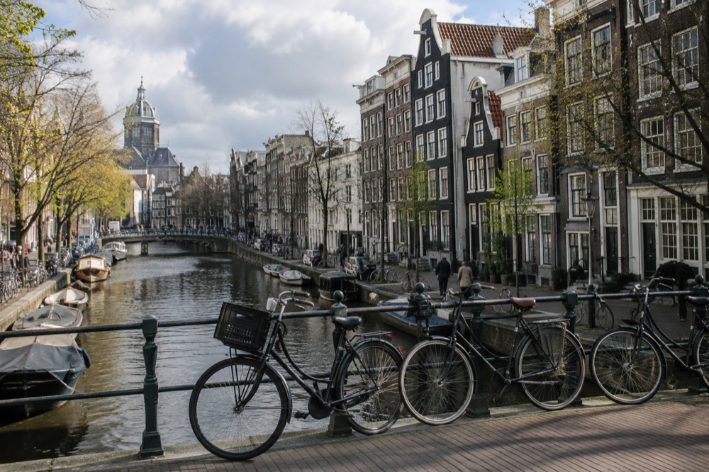 Bicycles leaning against a canal railing outside a row of narrow gabled houses