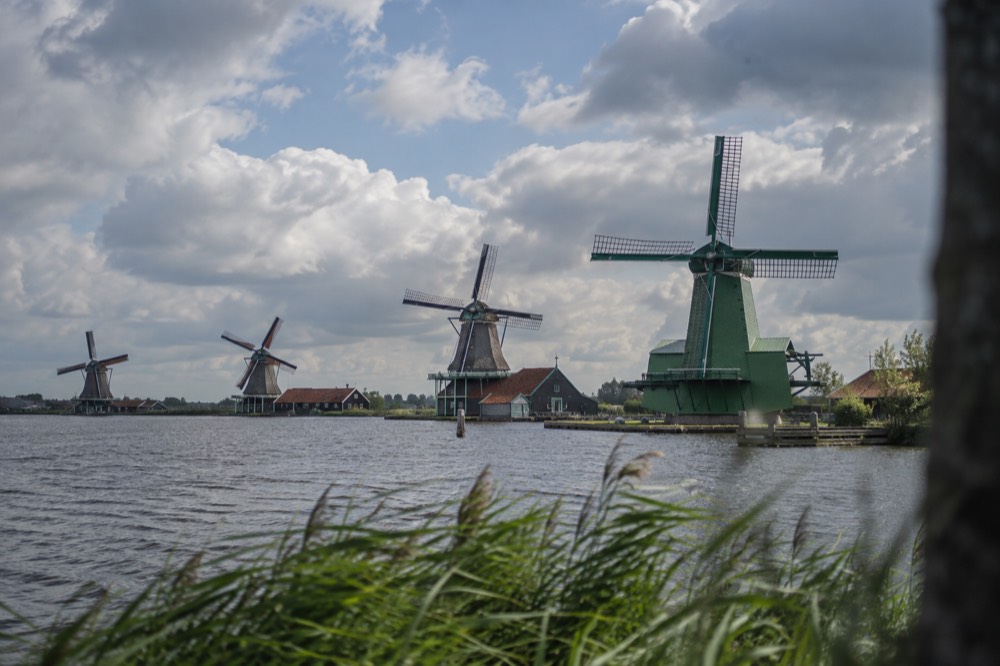 A row of working windmills beside water at Zaanse Schans under a wide sky