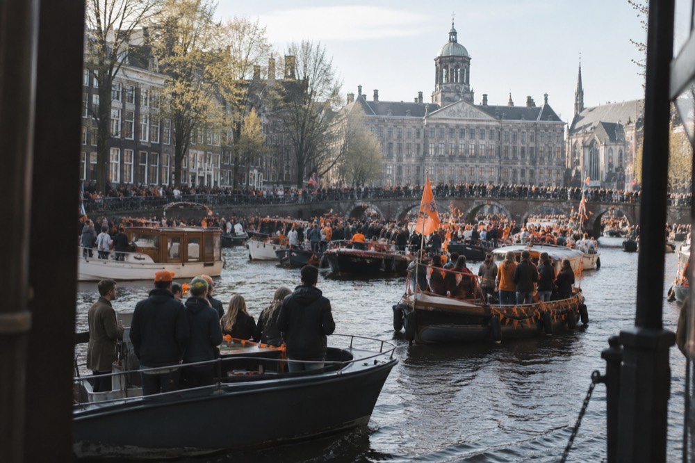 Boats crowded together on an Amsterdam canal flying orange flags during a spring festival