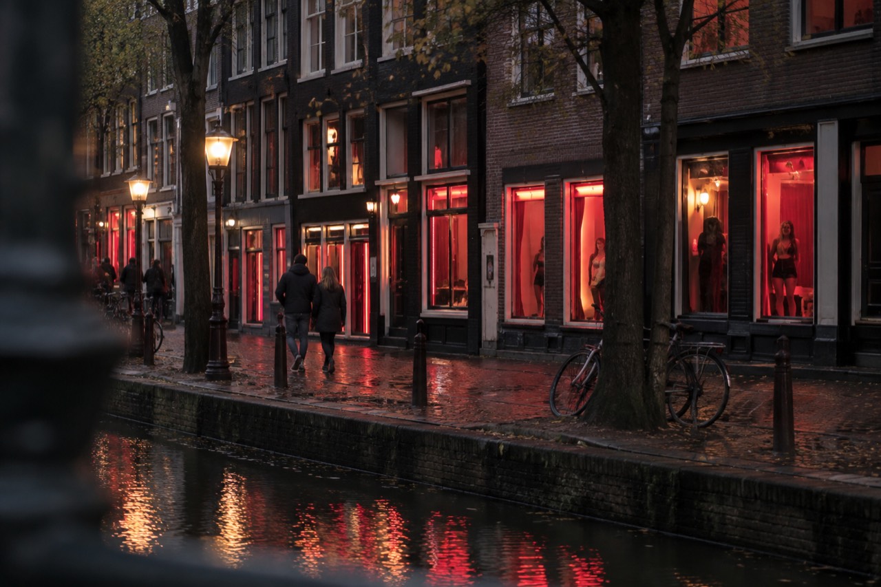 Narrow Amsterdam street at dusk with old brick buildings and warm window light reflecting on wet cobblestones