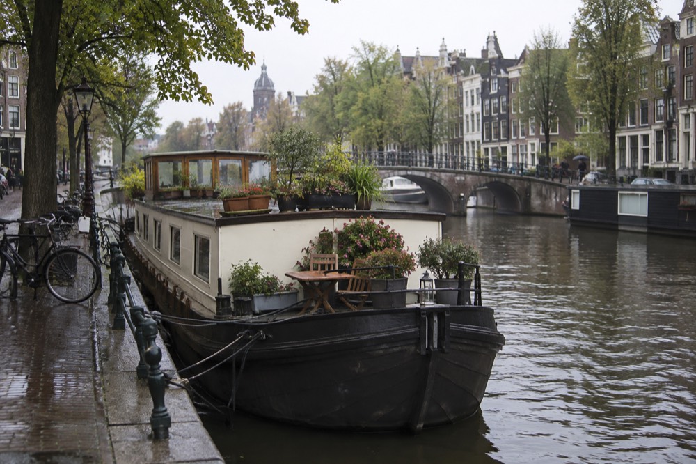 A converted houseboat moored on an Amsterdam canal with flower boxes on the deck