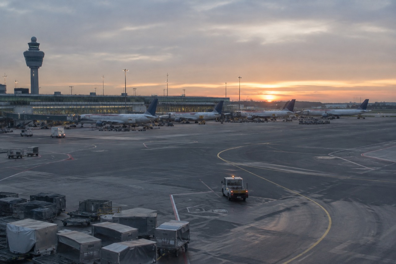 Airport terminal exterior at dusk with planes parked at gates and a taxiway in the foreground