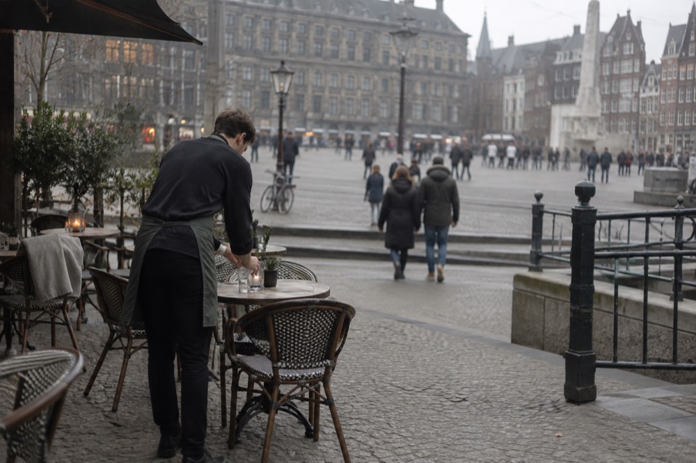 A waiter setting a small table outside a café on an Amsterdam canal street