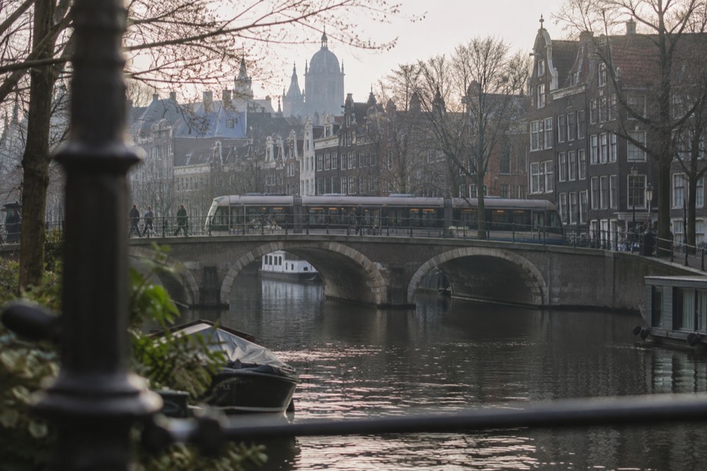 Trams crossing a stone bridge over an Amsterdam canal lined with narrow gabled houses