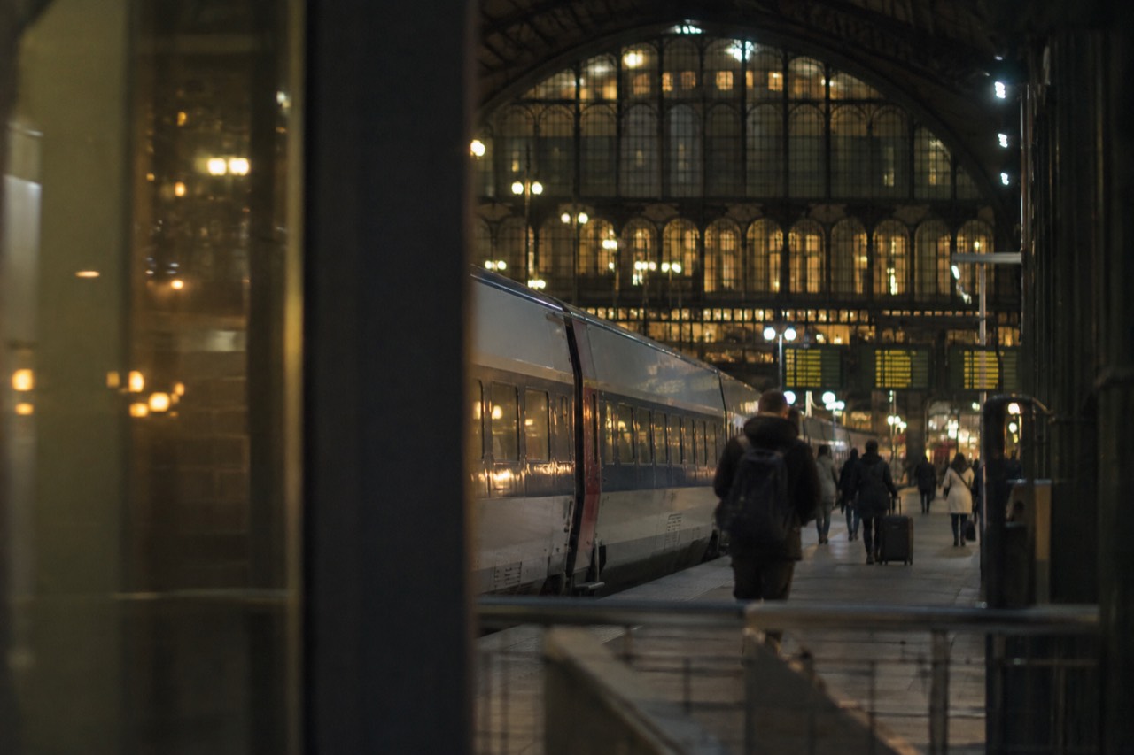 A long-distance train at a platform beside a station hall with departures boards