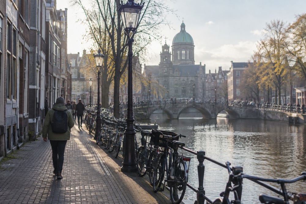 A rain-jacketed walker on a narrow canal-side street beside parked bicycles