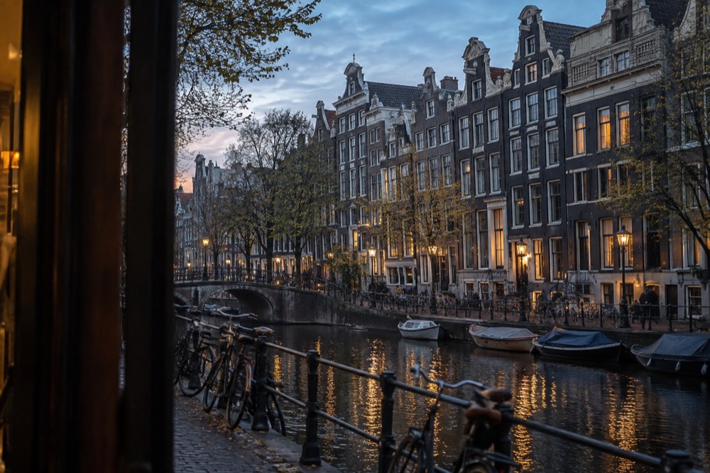 A row of tall narrow Amsterdam canal houses with gabled facades along a tree-lined canal