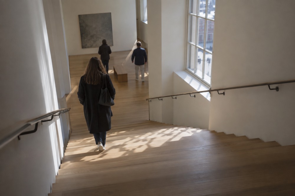 A quiet Amsterdam museum staircase with pale wood steps and daylight from a tall window