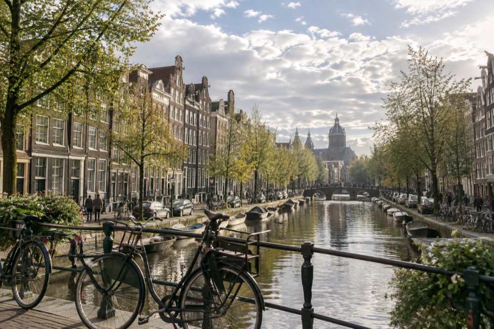 Amsterdam canal in morning light with rows of narrow gabled houses and parked bicycles on the quay