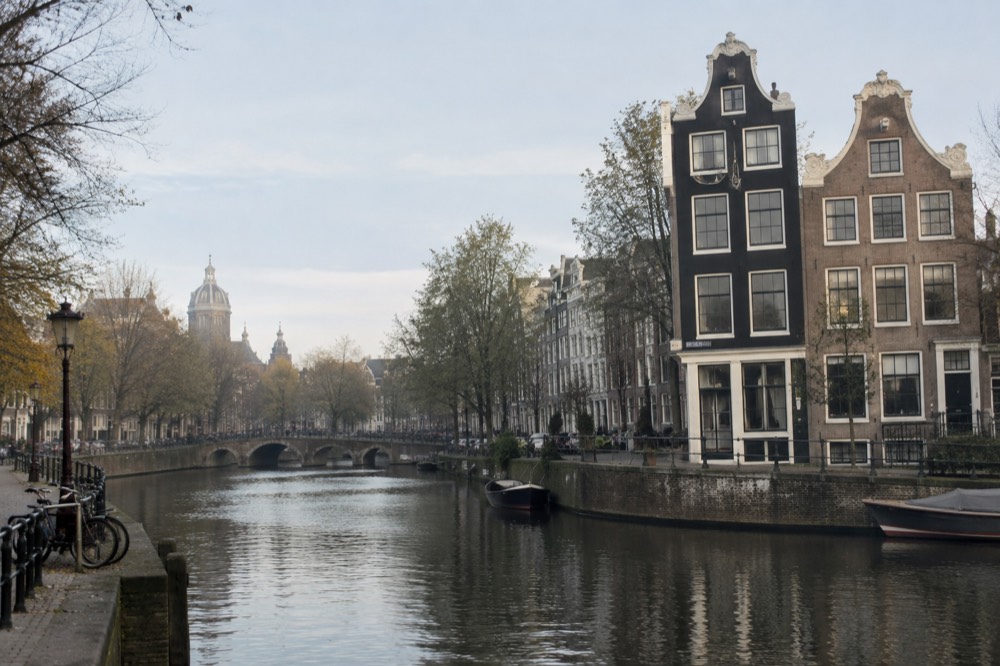 Two canal houses with gabled facades beside a quiet Amsterdam canal in morning light