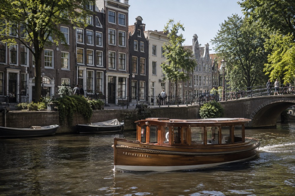 A classic wooden saloon boat passing gabled canal houses on an Amsterdam canal