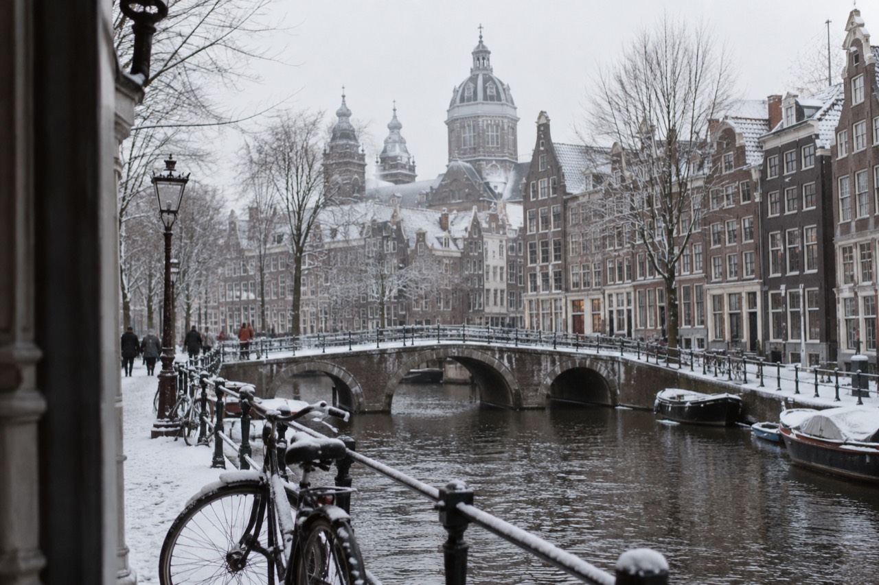 Amsterdam canal houses and bridges dusted with snow under a pale winter sky
