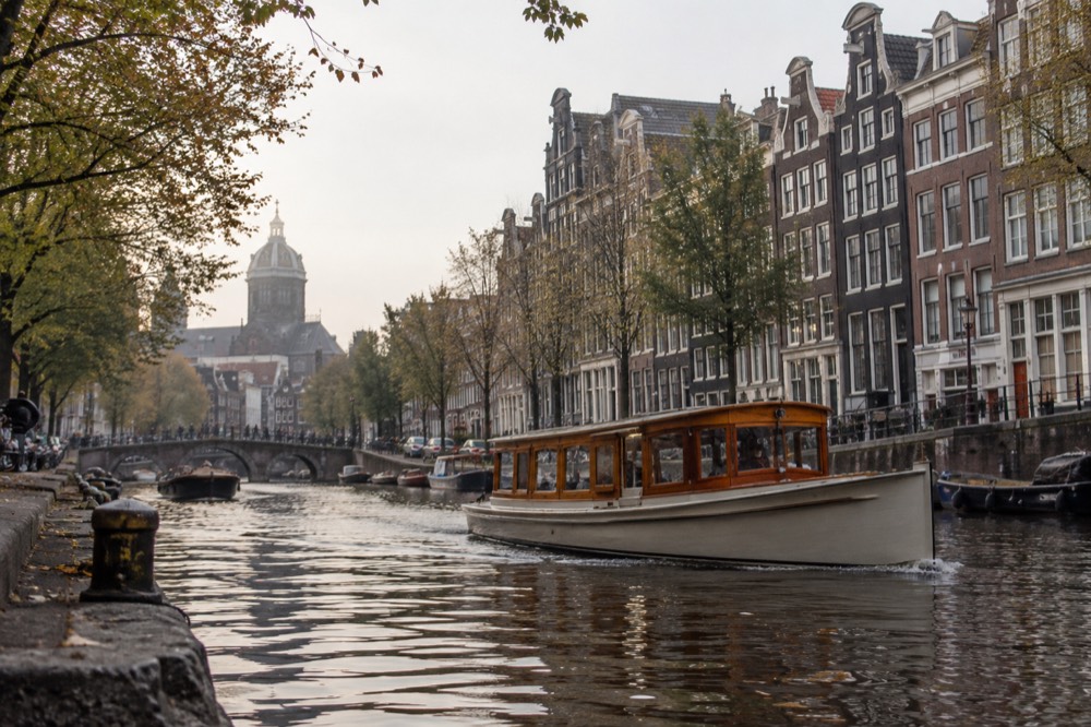 A classic wooden saloon boat cruising past narrow gabled canal houses