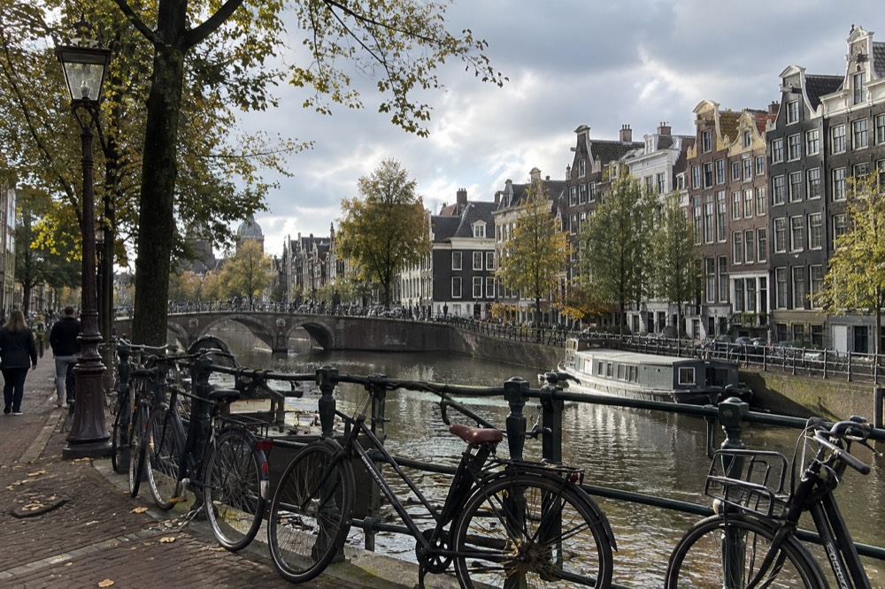 A row of tall narrow gabled canal houses along the Herengracht with bicycles chained to a bridge railing
