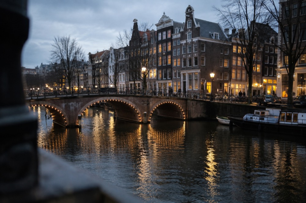 Illuminated Amsterdam canal bridge and gable ends reflected in dark water at night